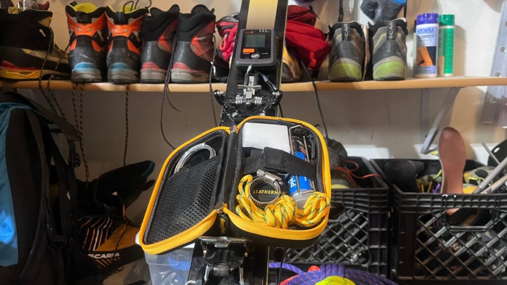 A backcountry ski repair kit and avalanche beacon on skis